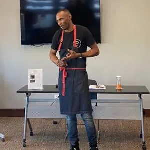 Chef Trillis Rollins in an apron giving a cooking demonstration